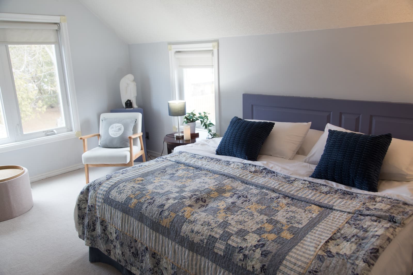 The Blue Room made up as a king bed, with a blue patchwork quilt and navy cushions against a slate-blue headboard beneath a sloped attic ceiling
